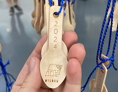 Kleiner gravierter Holzlöffel an einem blauen Band in einer Hand liegend