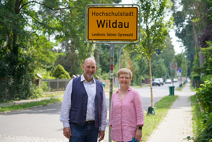 Wildaus Bürgermeister Frank Nerlich und TH-Wildau-Präsidentin Prof. Ulrike Tippe vor einem Ortseingangsschild der Hochschulstadt Wildau