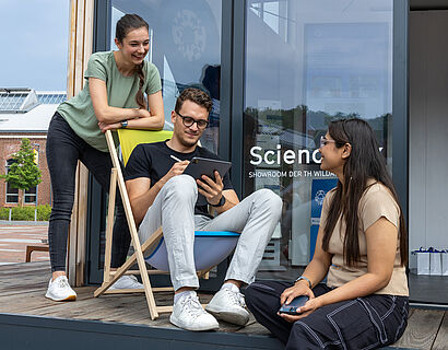 Drei Studierende sitzen und stehen vor der ScienceBox auf dem Campus der TH Wildau