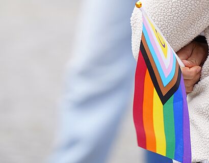 Nahaufnahme einer kleinen inter-inclusive Regenbogenflagge, die von einer Person in der Hand gehalten wird.