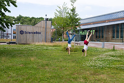 Zwei Studierende machen Handstand auf der Wiese vor Haus 16 auf dem Campus der TH Wildau