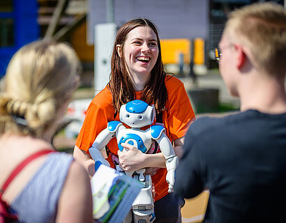 Studentin mit humanoidem Roboter auf dem Arm im Gespräch mit Besucherinnen und Besuchern des HIT 2024. 
