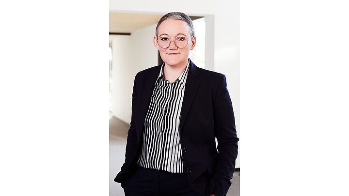 Medium Shot-Fotografie von Judith Muster in dunklem Anzug, die Hände in den Hosentaschen.