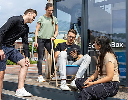 Studierende, sitzend und stehend, vor der ScienceBox auf dem Campus der TH Wildau