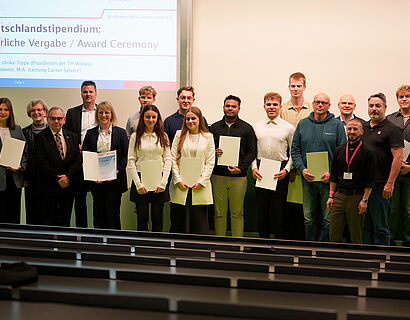 Personen stehen für ein Gruppenfoto zusammen und halten zum Teil Urkunden vor sich