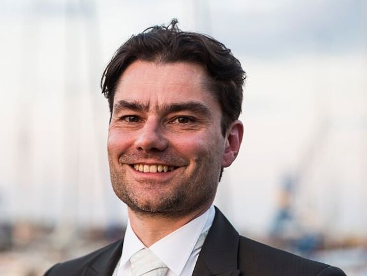 Auf dem Bild ist eine Person im Vordergrund zu sehen, diese Person lächelt, diese Person steht für eine Lunch and Learn-Reihe (Ein Schlungsformat) 