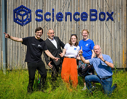 Jubelnde Beschäftigte der TH Wildau bei einem Gruppenfoto vor der ScienceBox.