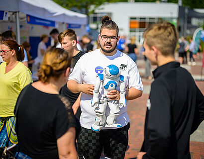 Student mit einem humanoiden Roboter im Arm im Gespräch mit Besucherinnen und Besuchern beim HIT 2024.