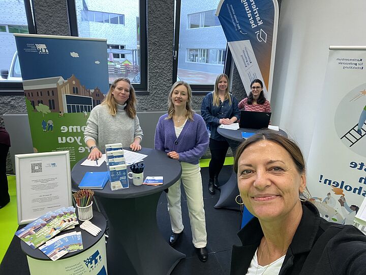 Foto eines Messestands der TH Wildau, aufgenommen als Selfie mit der Leiterin des Karrierezentrums im Bildvordergrund, im Hintergrund vier weitere Personen am Stand.