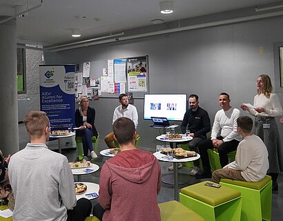 Rückenansicht von sechs Studierenden, die nach vorne auf vier Alumni schauen, die eine Präsentation zeigen.