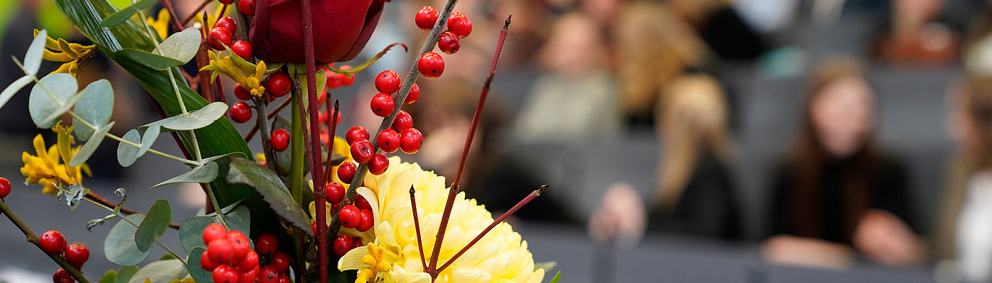 Blick auf einen Blumenstrauß mit Publikum im Hintergrund bei der feierlichen Verabschiedung der Absolventinnen und Absolventen 2023 des Fachbereichs WIR