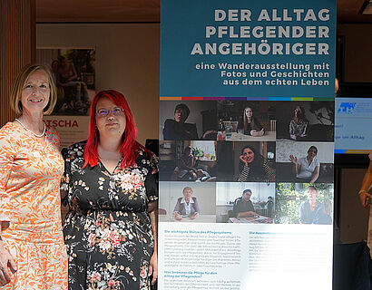 Zwei Frauen stehen neben einem Rollup mit der Aufschrift "Der Alltag pflegender Angehöriger"